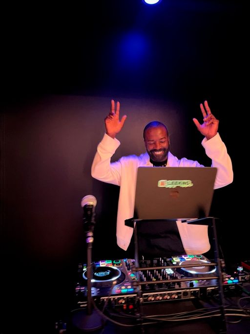 The DJ at the decks during a class, both hands up.