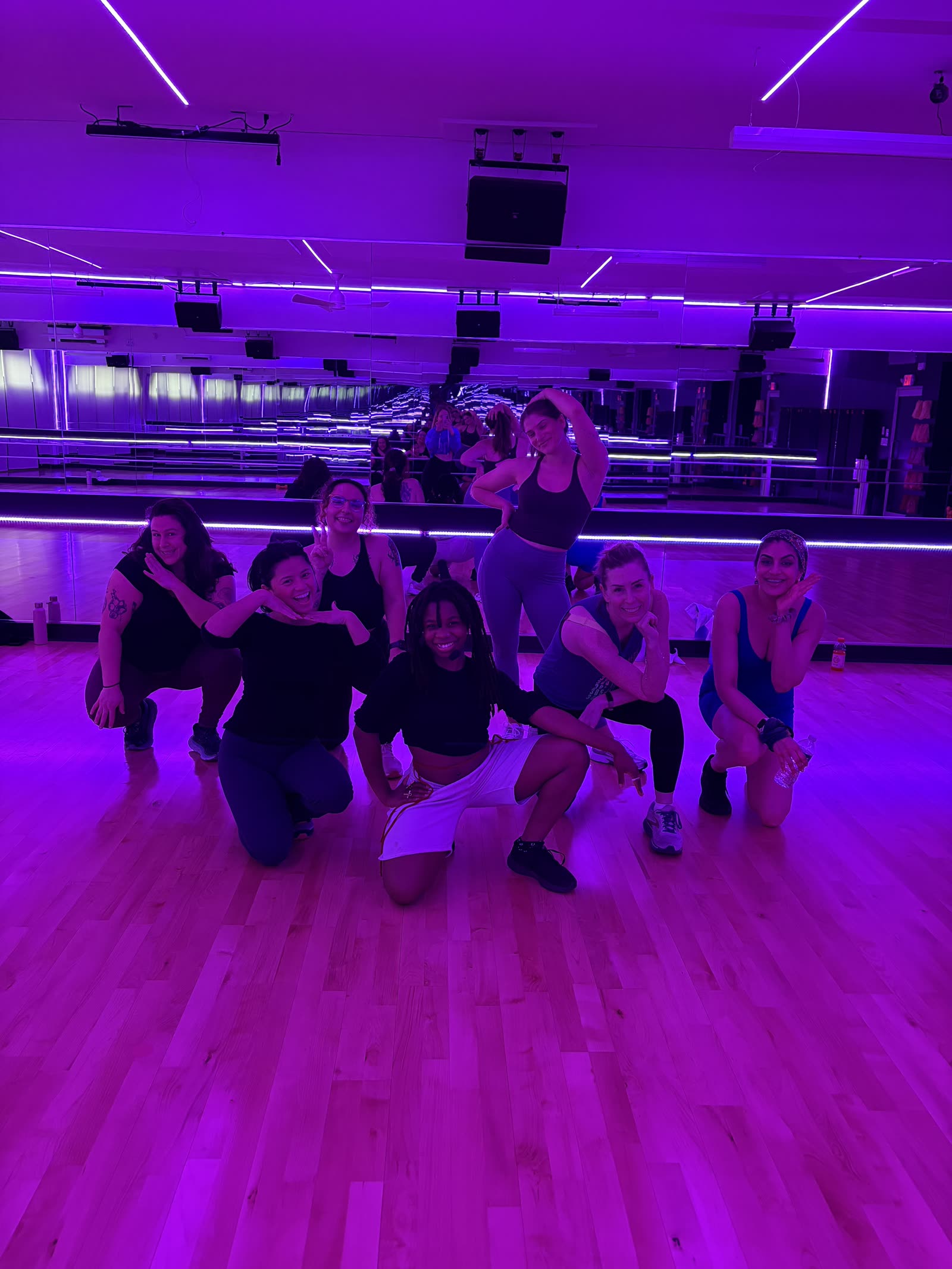A group of 305 Fitness Philly dancers crowded together on the studio floor under purple light, laughing after class.