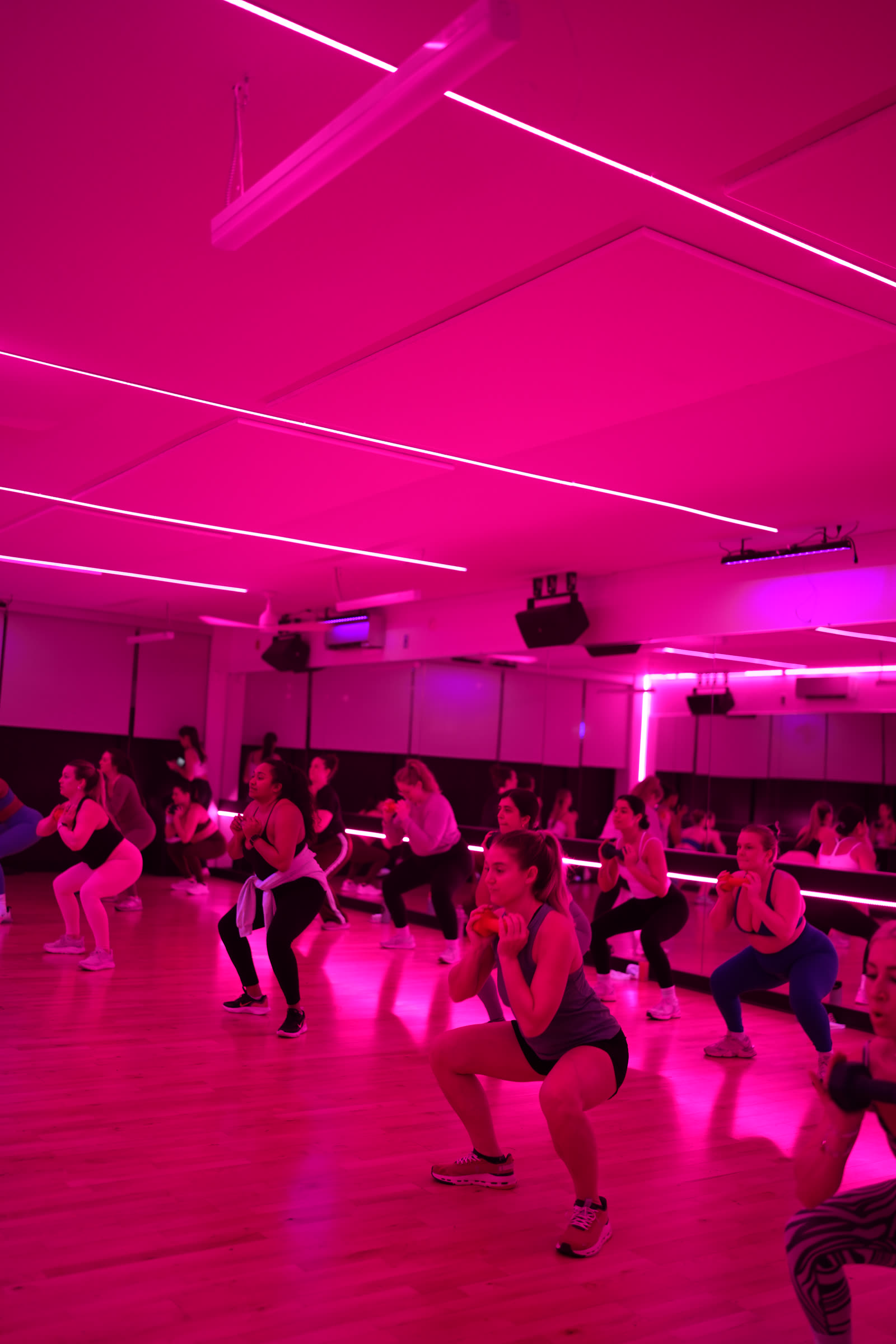 A packed 305 Fitness Philly studio under deep pink light, the whole class dropped into the same low squat mid-routine.